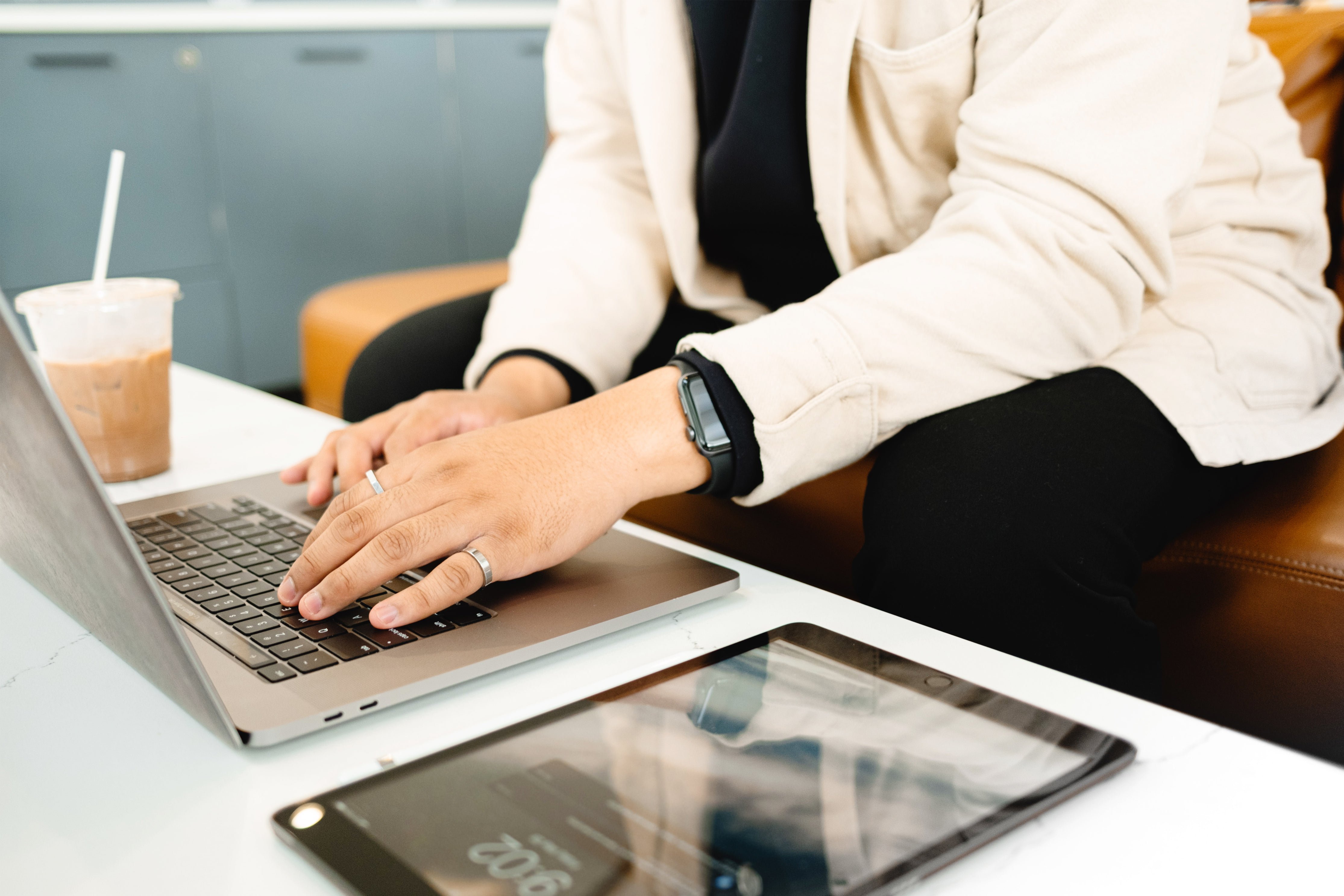 hands-type-on-a-laptop-next-to-iced-coffee-and-a-tablet
